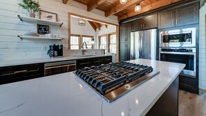 Een moderne keuken met een groot schiereiland, roestvrijstalen apparatuur, houten balken in het plafond en een witte achterwand.
