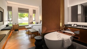 Habitación de hotel moderna con una cama grande, un área de descanso con vistas, un baño con bañera y un espejo amplio.