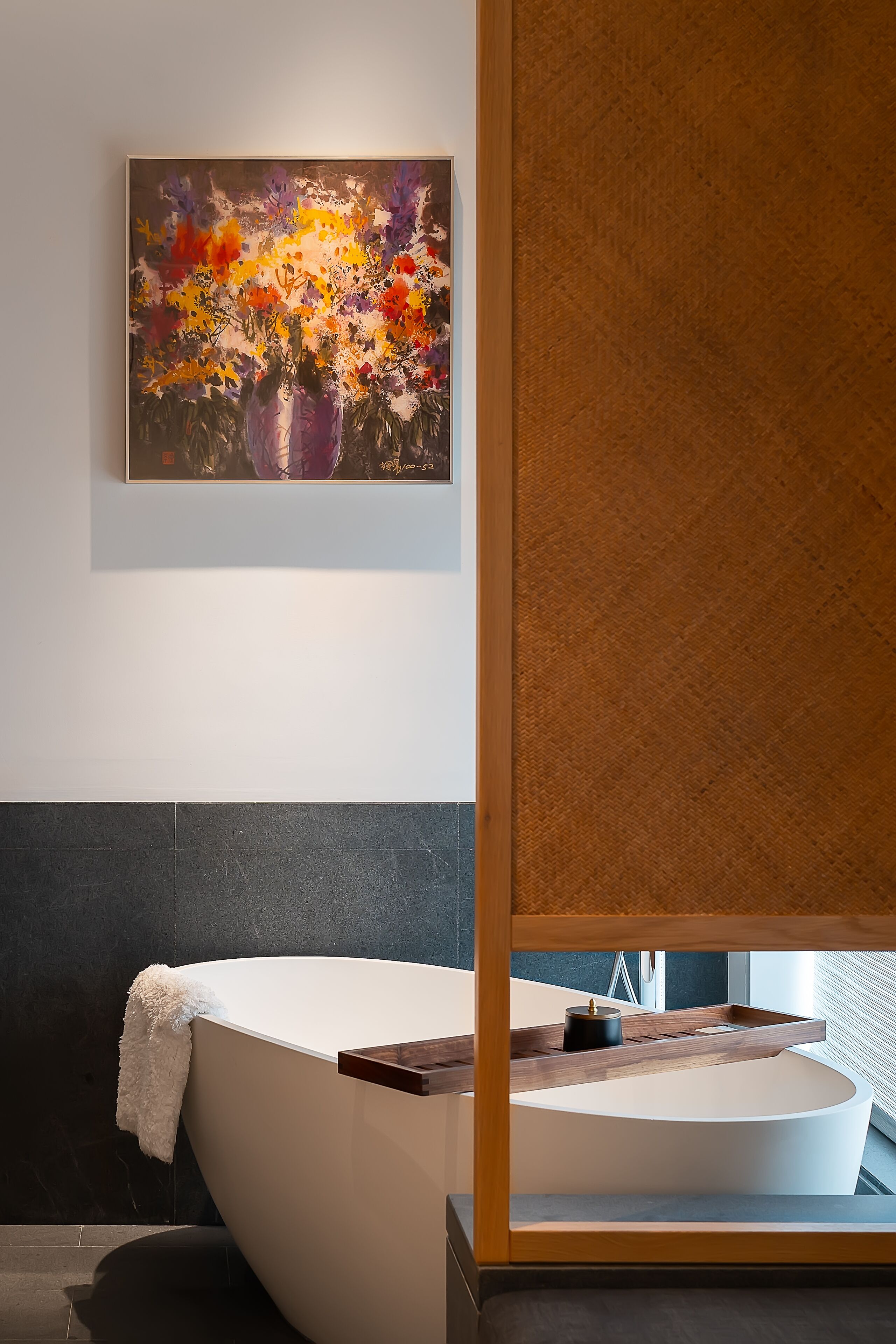 Ein modernes Badezimmer mit einer freistehenden Badewanne, einem Holztablett und einem Bild an der Wand.