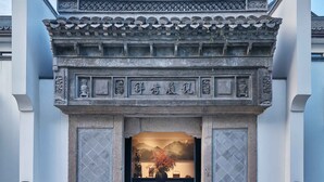 Entrada de un edificio tradicional chino, con tejado de tejas, arco de piedra y una pequeña mesa con un florero en su interior.