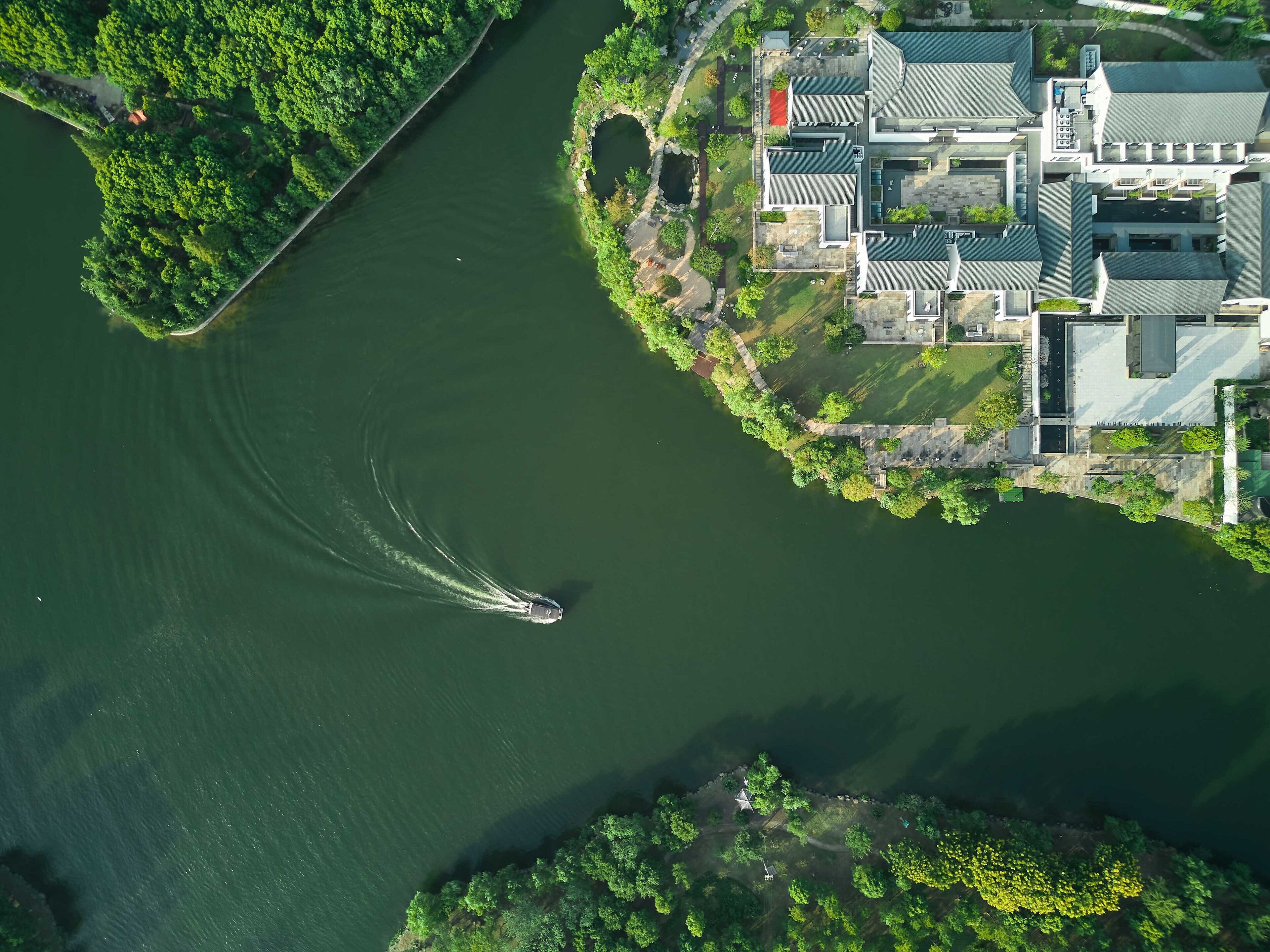 An aerial view of a riverside property with a boat creating a wake.