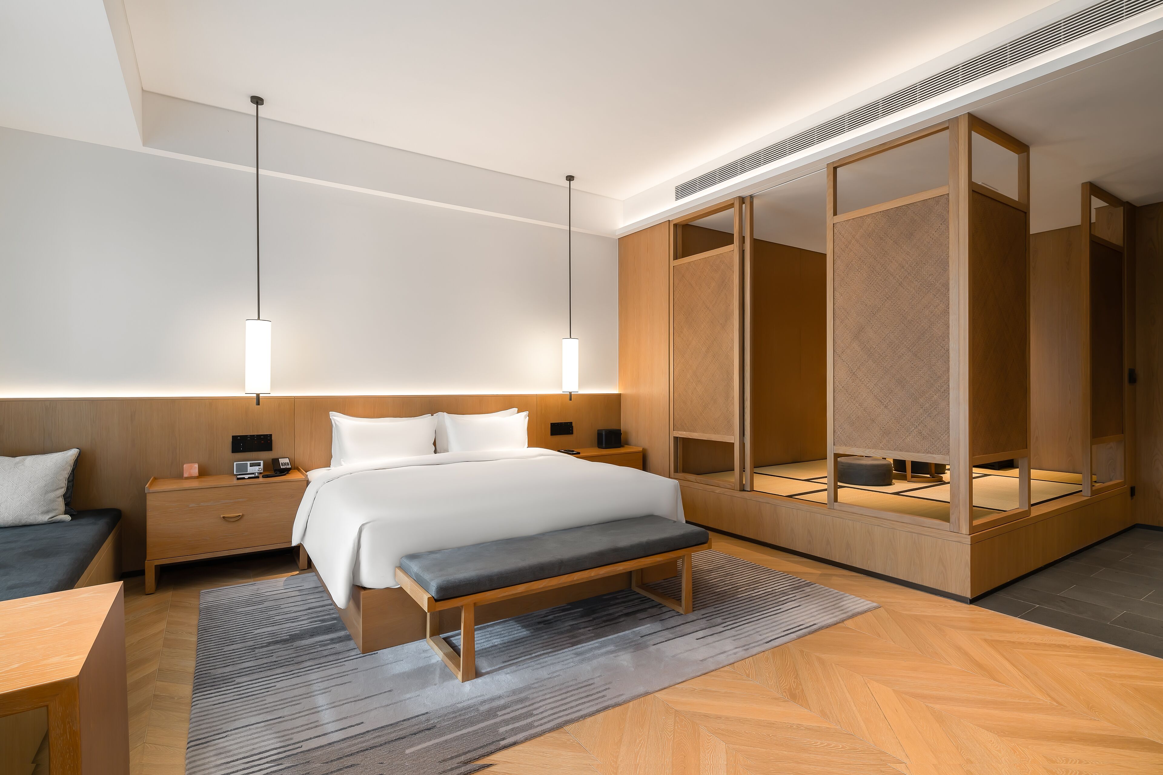 A modern hotel room with a large bed, bedside tables, a bench, and a wardrobe with a mirror.