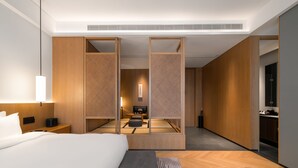 Una habitación de hotel moderna con una cama grande, un escritorio, una zona de estar y vistas a través de un separador.