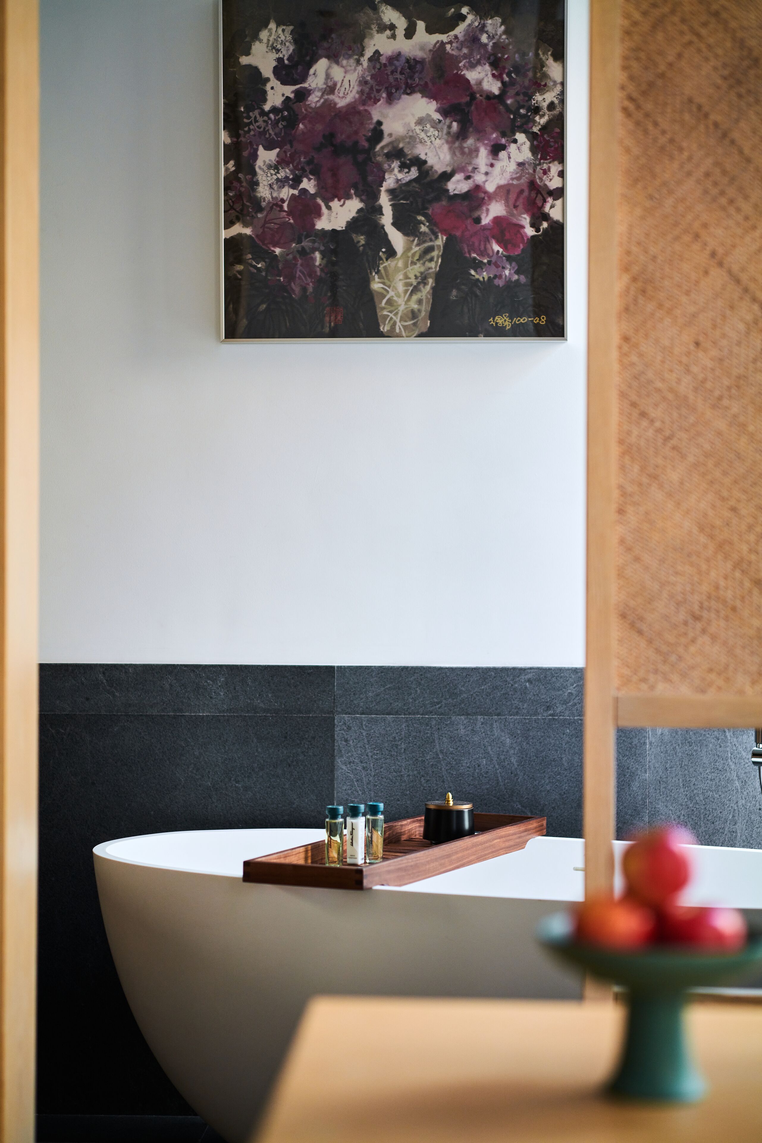 Un bagno moderno con una grande vasca da bagno bianca, un vassoio di legno con bottiglie e una ciotola di frutta su un tavolo.
