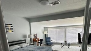 Quarto de hotel moderno com uma cama grande, uma escrivaninha, uma cadeira, uma televisão e uma janela com persianas.