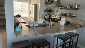 Uma cozinha moderna com uma bancada grande, banquetas e forno embutido.