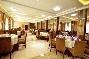 Ein Speisesaal eines Hotels mit runden Tischen, Stühlen und einer Kristallleuchter.