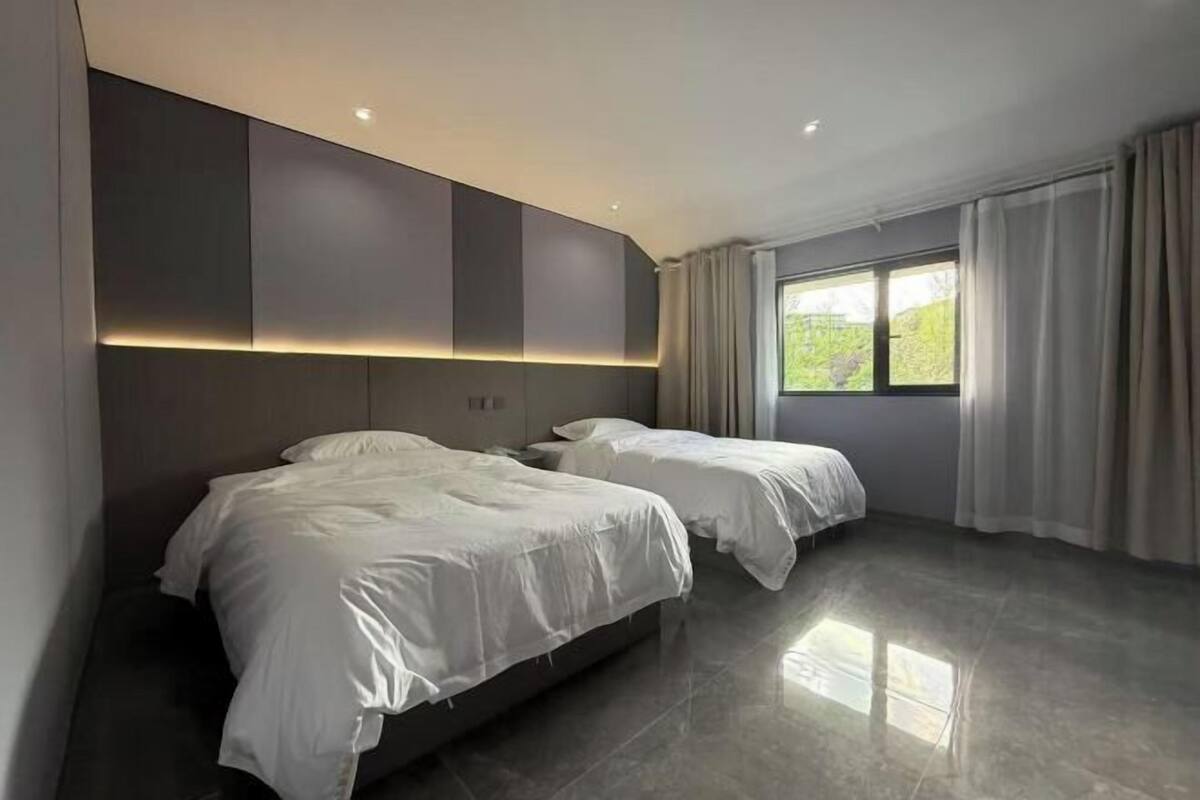 Un dormitorio moderno con dos camas, un ventanal con cortinas y un panel de luz en la pared.