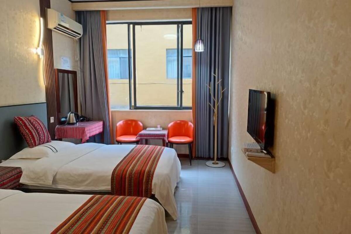 Habitación de hotel con dos camas, televisión, una mesita, dos sillas y una ventana con cortinas.