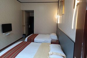 Habitación de hotel con dos camas, un televisor y una puerta que da a un pasillo.