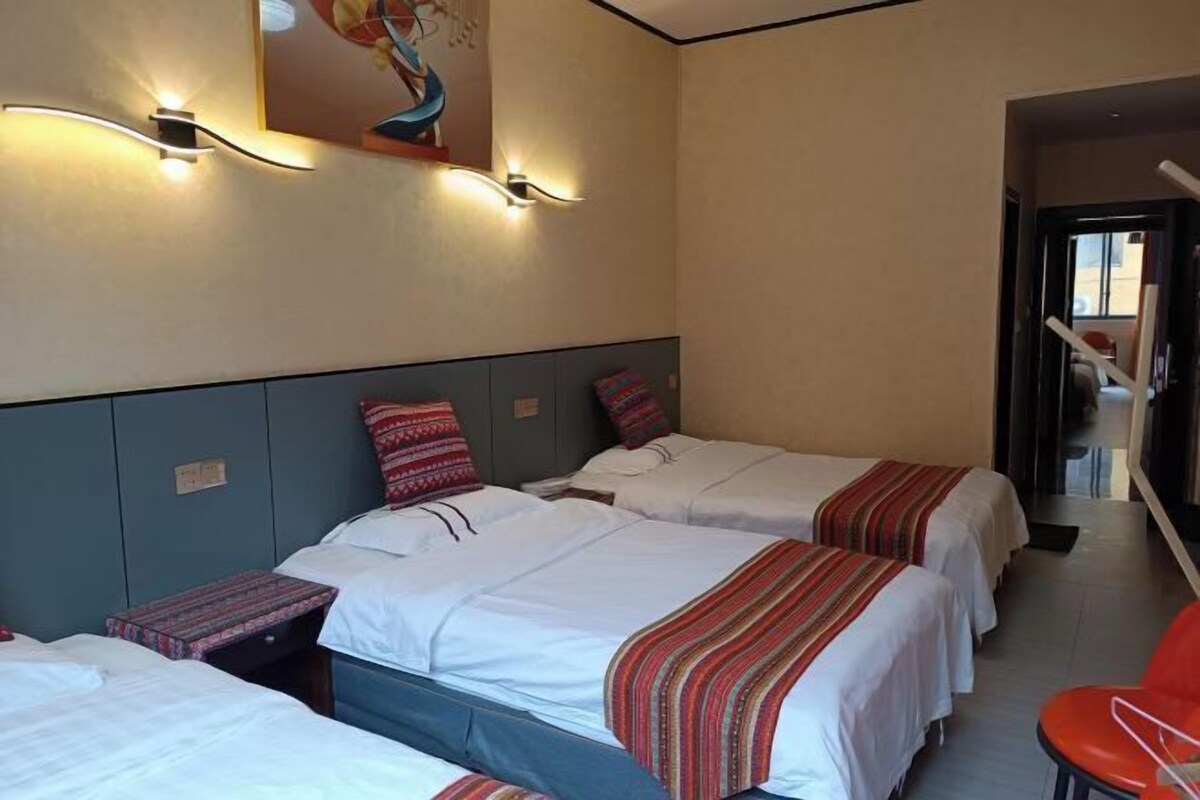 Habitación de hotel con tres camas, una silla roja e iluminación en la pared.