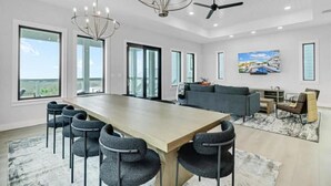 Een ruime woonkamer met een grote houten tafel, meerdere stoelen, een bank en een plafondventilator.