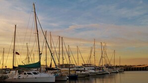 Un port de plaisance où sont amarrés de nombreux voiliers, sur une eau calme, au coucher du soleil.