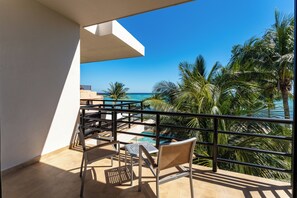 A balcony with a view of the ocean, a pool, and palm trees.