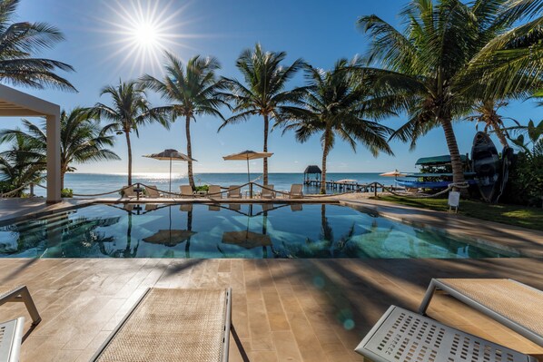 A poolside area with lounge chairs, umbrellas, and palm trees.