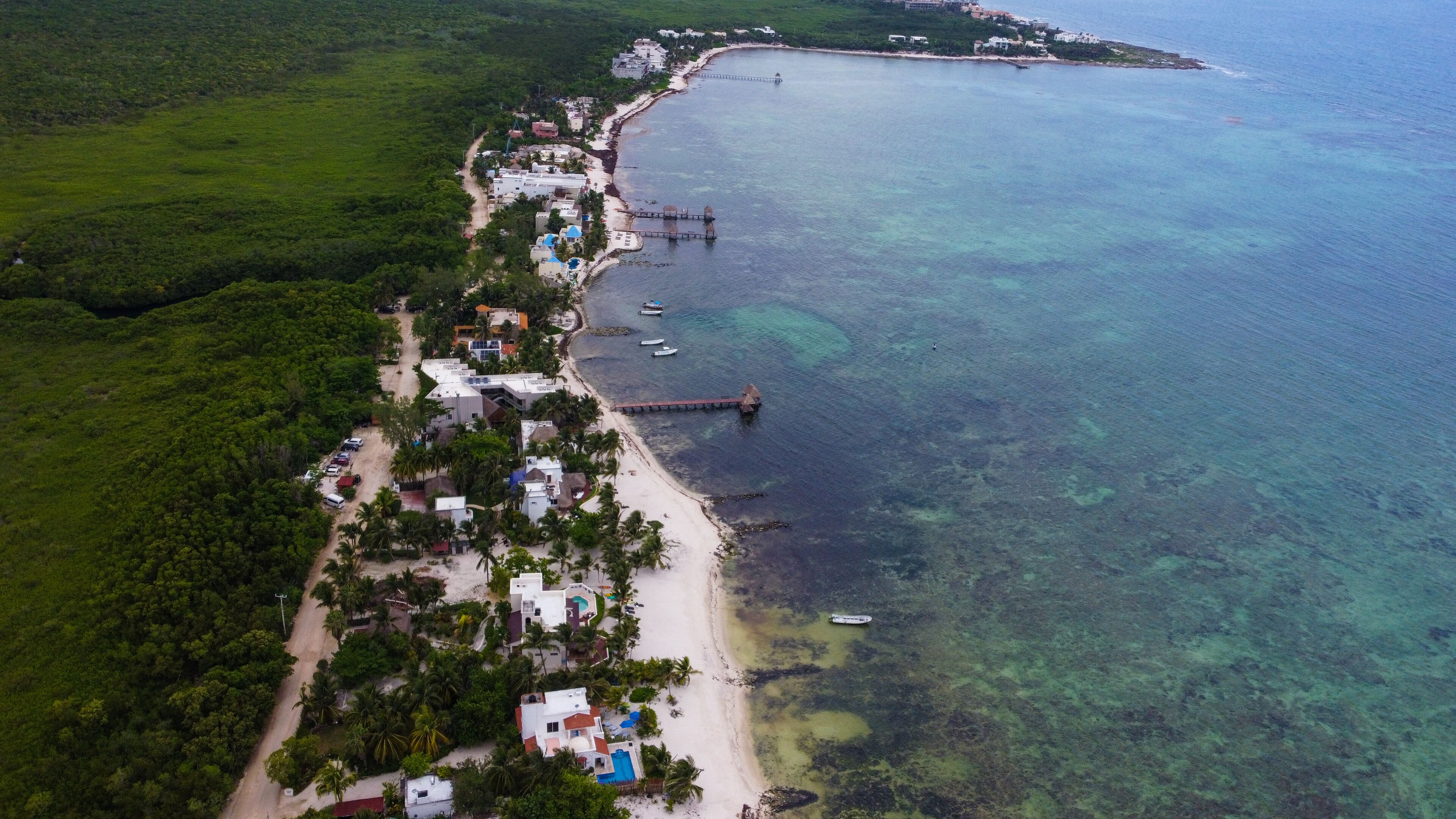 Vista aérea de una zona costera con playa, aguas claras y un muelle.