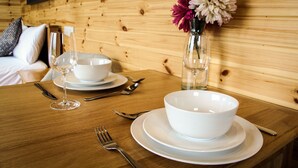 A wooden dining table set with white plates, bowls, cutlery, and a vase with flowers.
