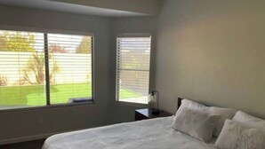 A bedroom with a large bed, two windows, and a nightstand.