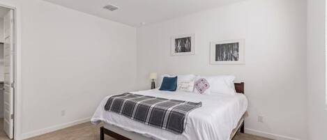 A bedroom with a bed, a door, and two framed pictures on the wall.