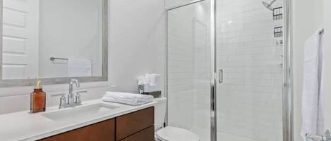 A modern bathroom with a glass-enclosed shower, a white toilet, and a vanity with a mirror and a sink.
