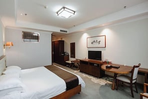 Ein Hotelzimmer mit Bett, Schreibtisch, Stuhl, Fernseher und einem gerahmten Bild an der Wand.