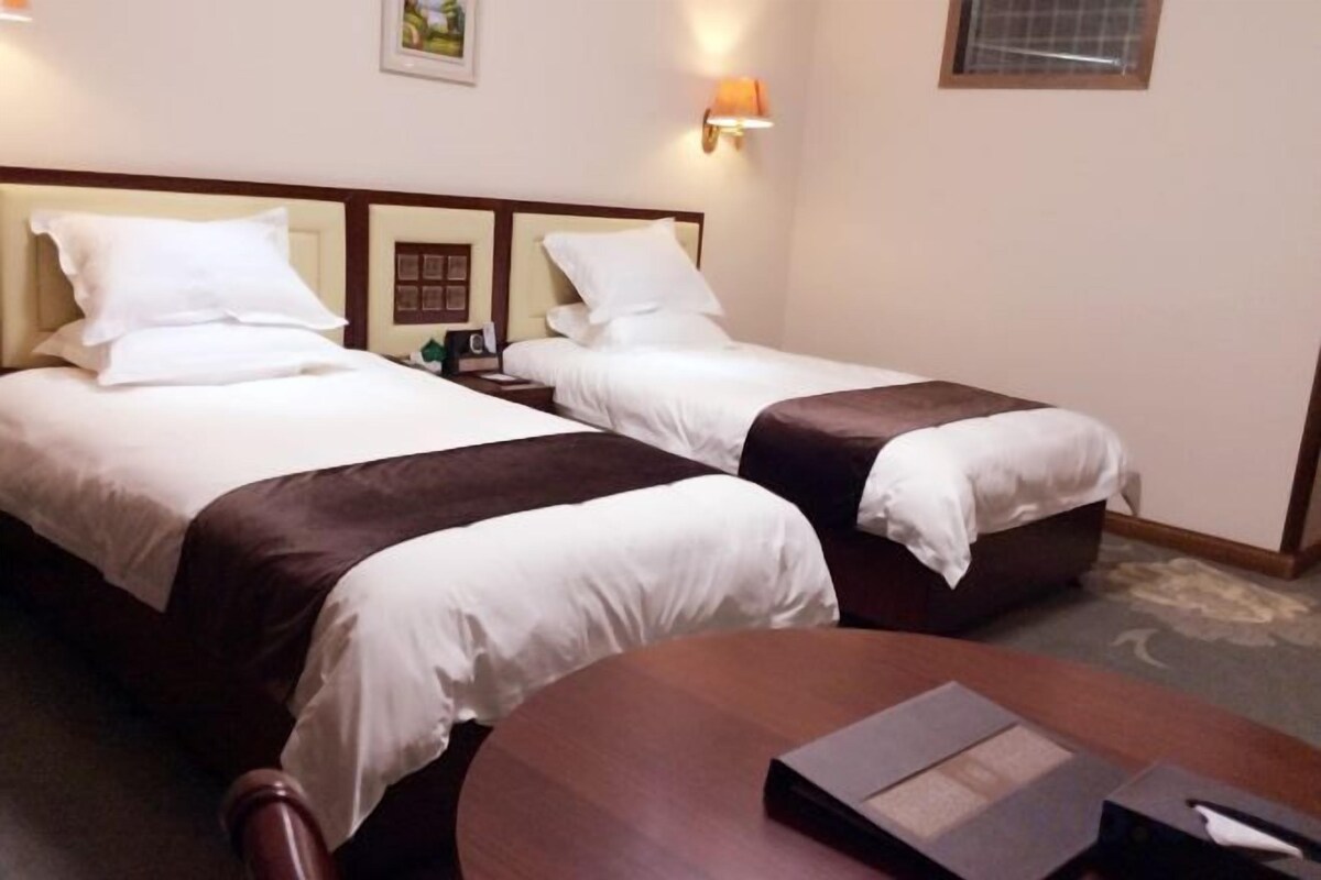A hotel room with two beds, a wooden table, and a nightstand with a lamp.