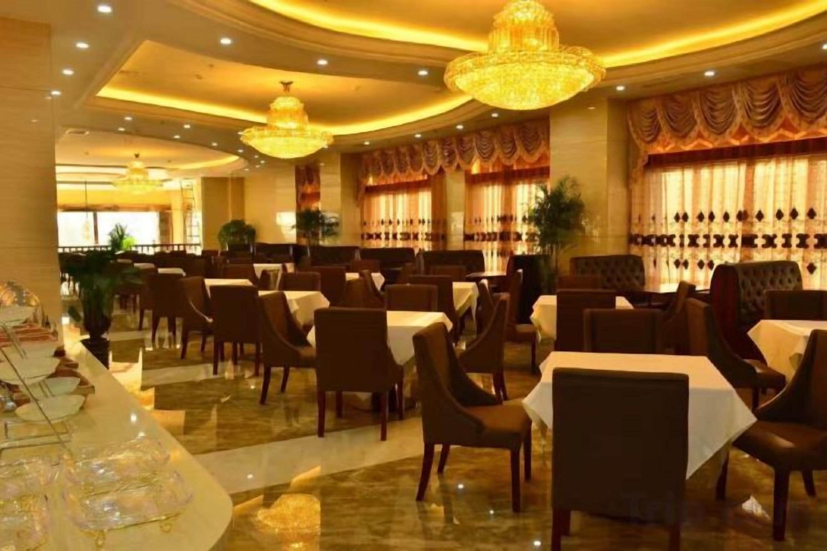 A restaurant with multiple tables and chairs, chandeliers, and curtains.