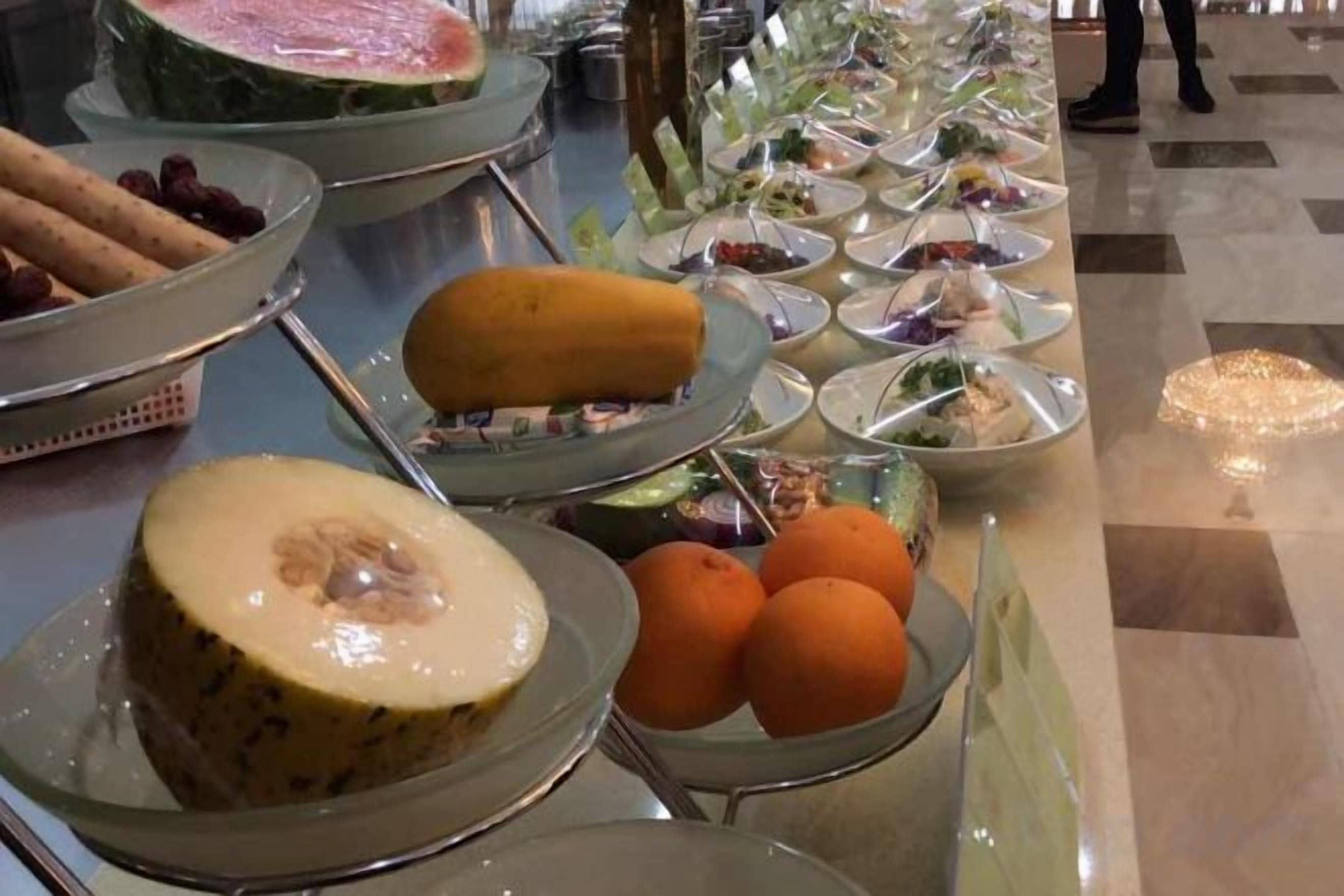 Un bufé con diversos alimentos, incluyendo frutas, verduras y un melón grande.