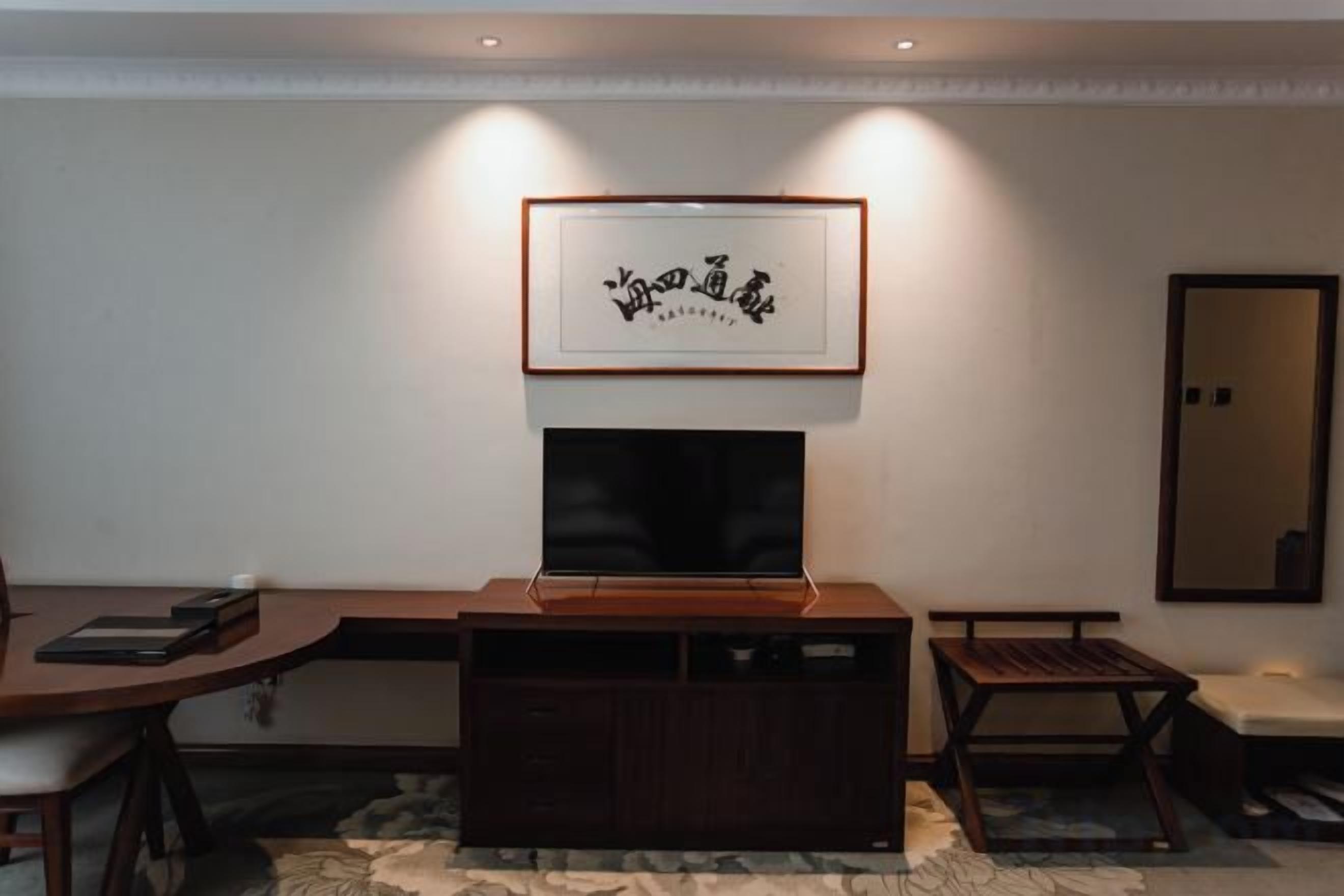 Un salon avec un téléviseur à écran plat fixé au mur, un meuble de rangement en bois et une œuvre d’art encadrée au-dessus du téléviseur.