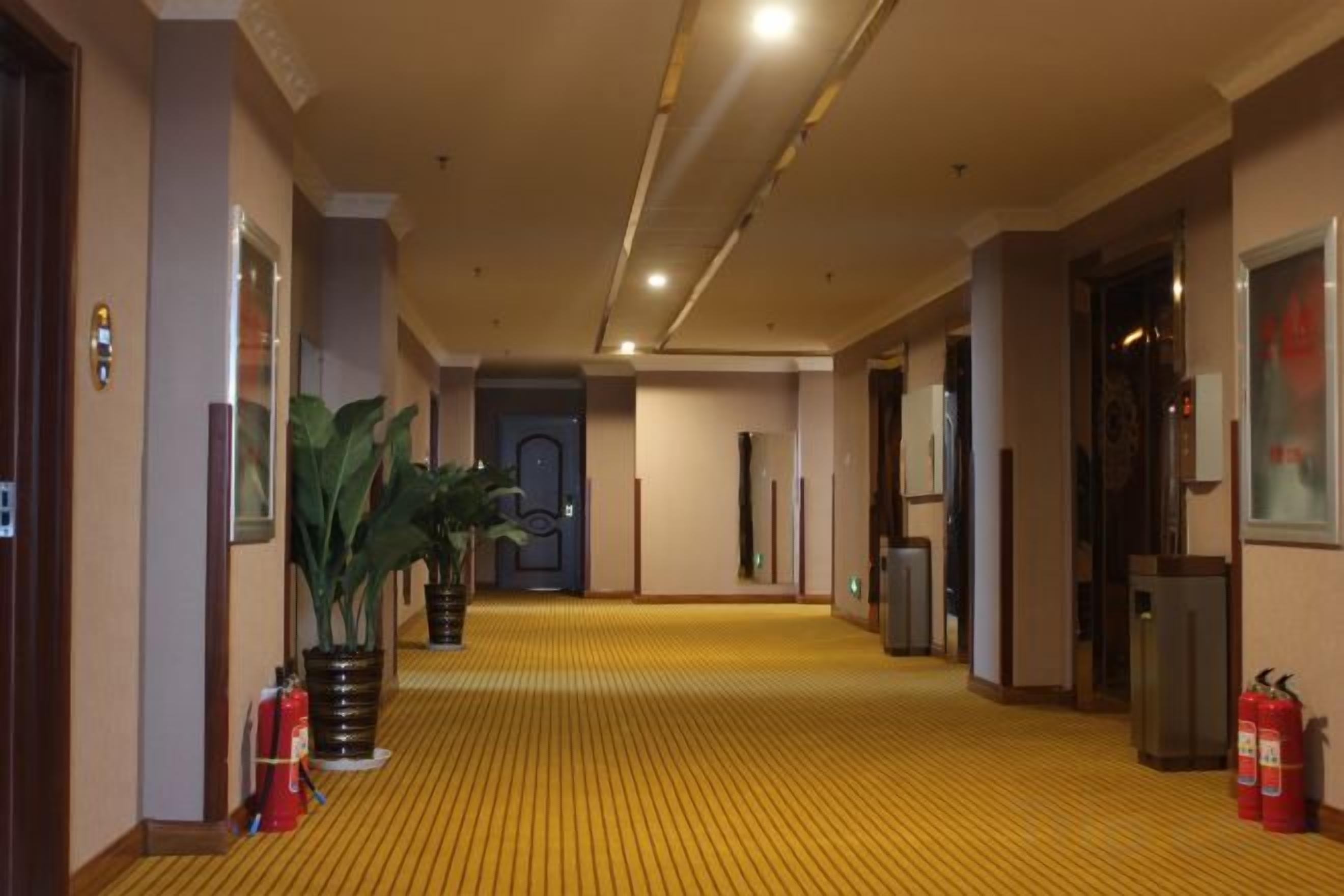 Un corridoio di un hotel con tappeto giallo, estintori e una porta in fondo.