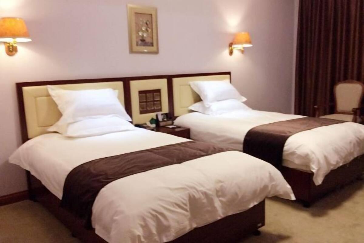 A hotel room with two single beds, each with a headboard, bedside tables, and lamps.