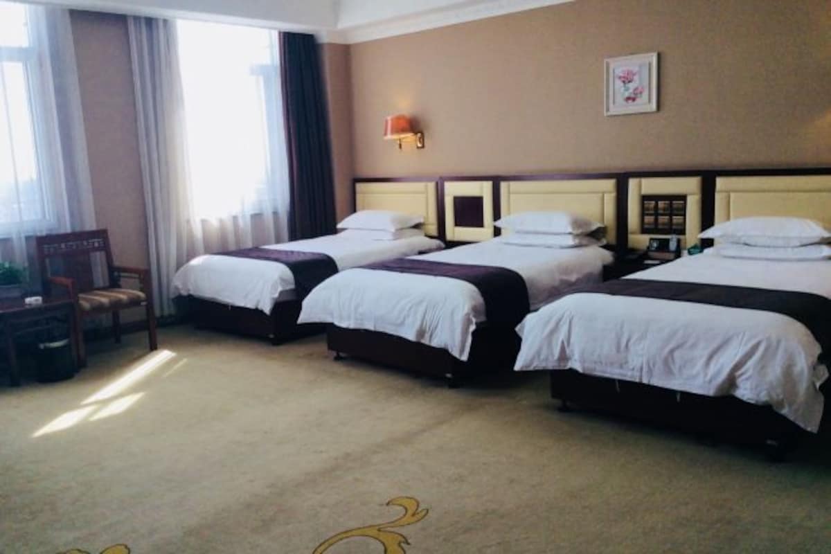Ein Hotelzimmer mit drei Einzelbetten, einem Schreibtisch und einem Stuhl.