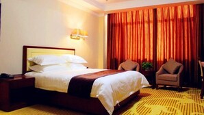 Habitación de hotel con una cama grande, una mesita de noche, dos sillas y una ventana con cortinas.