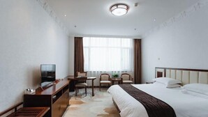 Habitación de hotel con cama, escritorio con silla, televisión y ventana con cortinas.