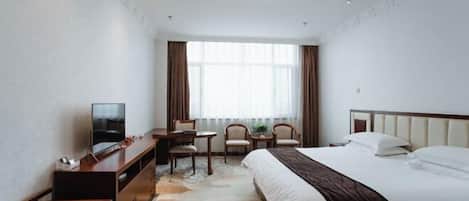 A hotel room with a bed, a desk with a chair, a television, and a window with curtains.