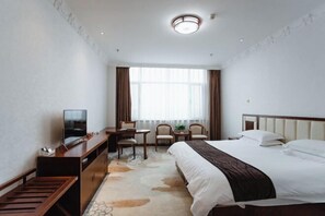 Une chambre d’hôtel comprenant un lit, un bureau avec une chaise, une télévision et une fenêtre avec des rideaux.
