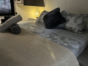 Un lit bien fait, avec une couvre-lit à motifs et des oreillers, une lampe de chevet et une couverture de couleur foncée.