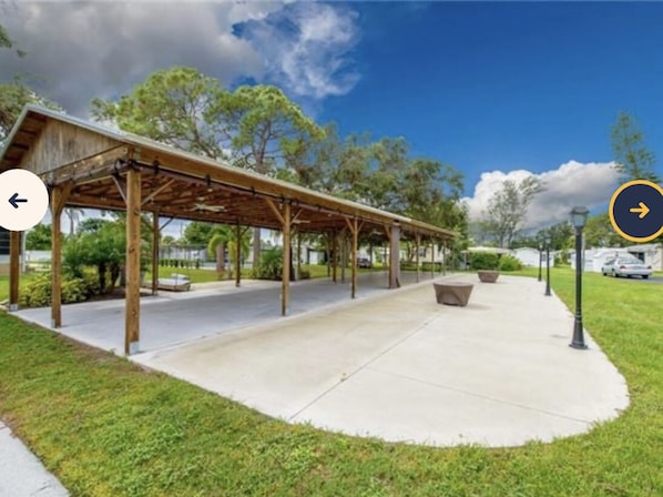 Un espace extérieur abrité, doté d’un sol en béton, de bancs et d’une structure de pergola en bois.