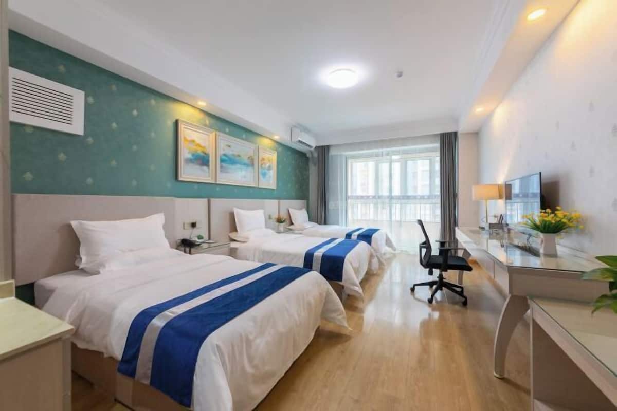 A hotel room with two beds, a desk, a chair, and a TV.