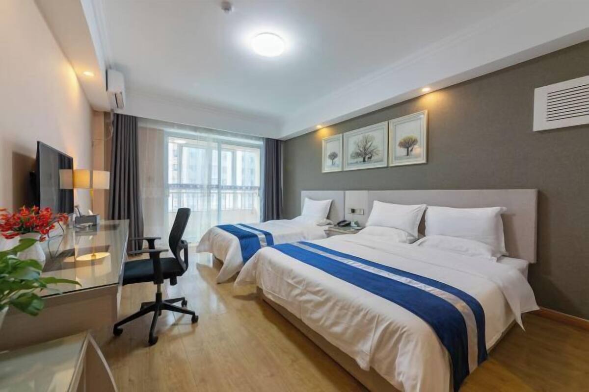 A hotel room with two beds, a desk with a chair, a TV, and a window with curtains.