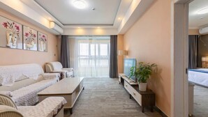 A modern hotel room with a sofa, a TV, a small table, and a potted plant.