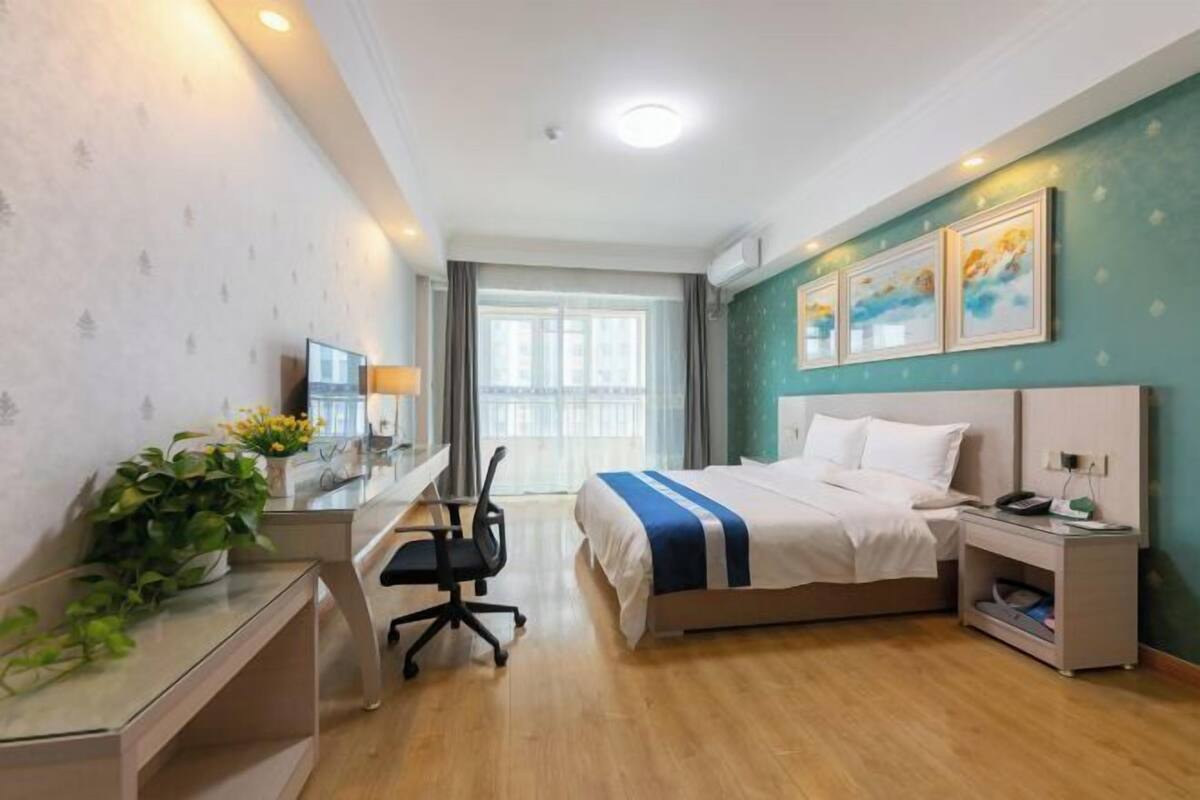 A hotel room with a bed, desk, chair, bedside table, and a window.