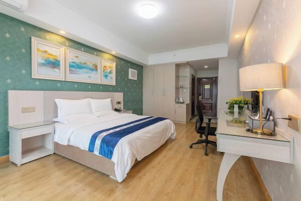 A hotel room with a bed, bedside table, desk, lamp, and artwork on the wall.