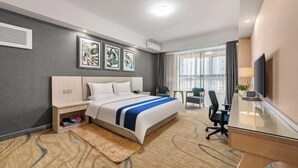 A hotel room with a bed, desk, and chair, a large window, and artwork on the wall.