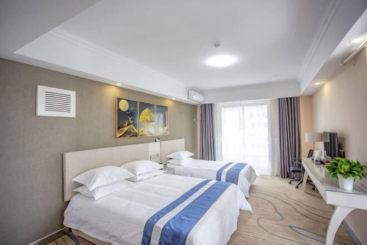 A hotel room with two beds, a desk, a TV, and a window with curtains.