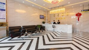 A hotel lobby with a reception desk, two sofas, a coffee table, and a chandelier.