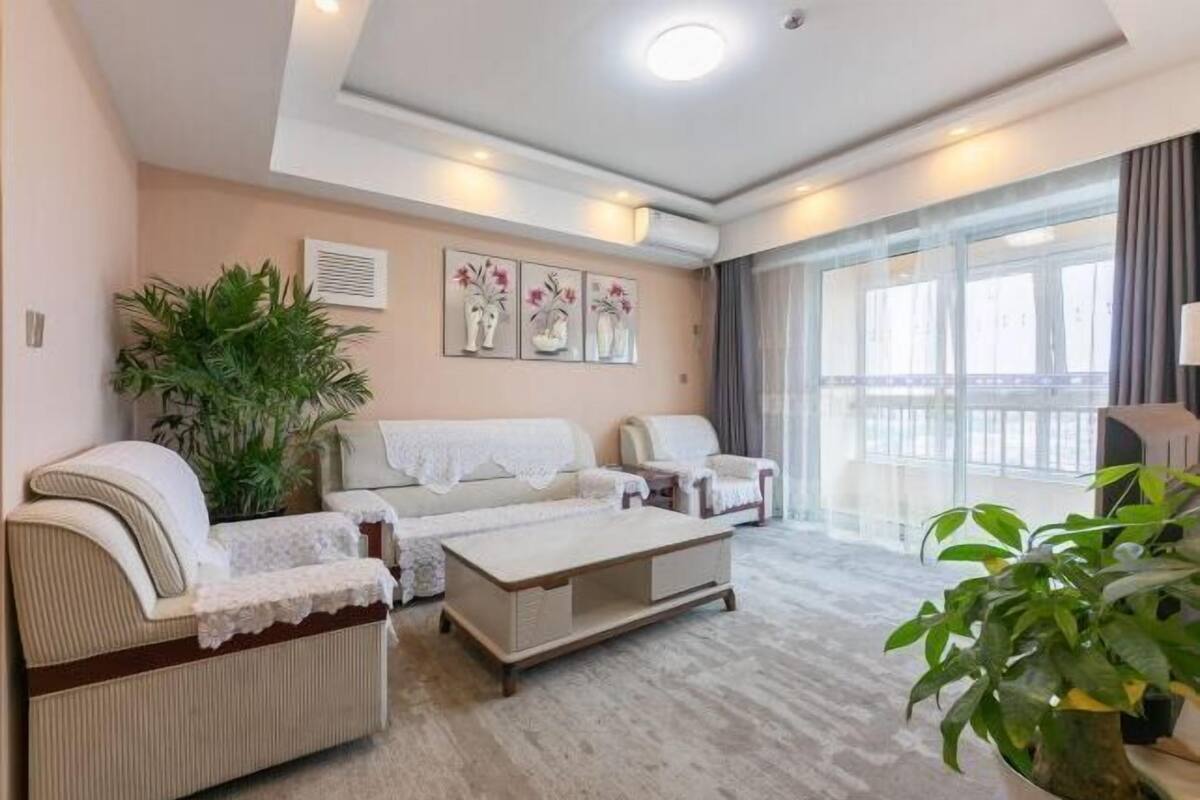 A spacious living room with a sofa, armchairs, a coffee table, and a large window with curtains.