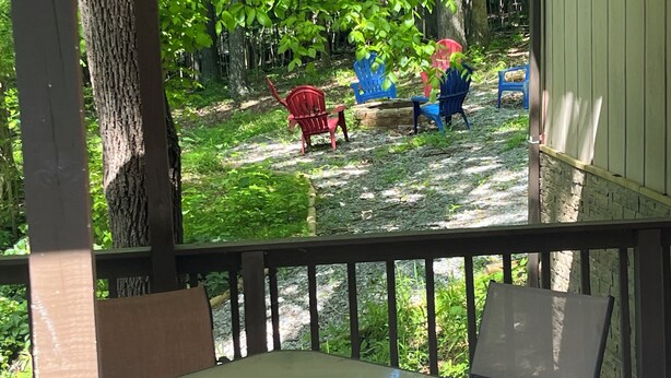 A covered outdoor seating area with a table and chairs, surrounded by trees and a stone wall. - Brown House in the Woods - Barkley Lake Area (Cadiz)