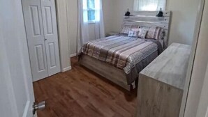 A bedroom with a bed, a dresser, a window with curtains, and a door. - Brown House in the Woods - Barkley Lake Area (Cadiz)