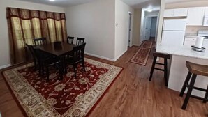 A dining area with a wooden table and chairs, a red and beige patterned rug, and a kitchen with white cabinets and a countertop. - Brown House in the Woods - Barkley Lake Area (Cadiz)